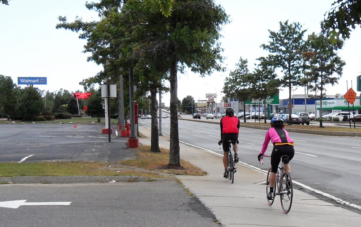 Photo of bicyclists riding on sidewalk next to three traffic lanes